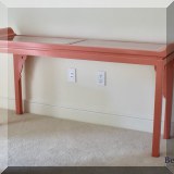 F66. Salmon colored Asian-inspired console table with glass top. 31”h x 63”w x 15”d 